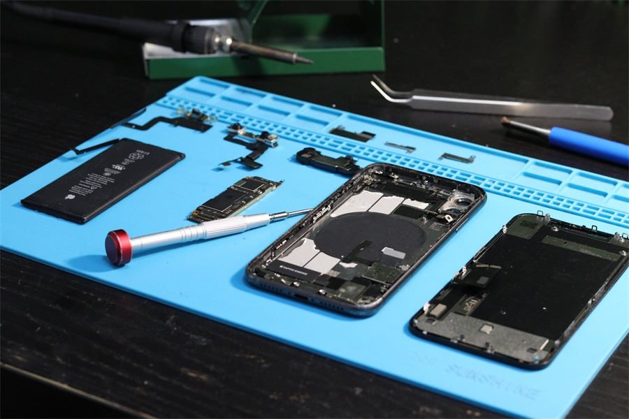 Reparación de celular con batería, placa y herramientas sobre tapete antiestático